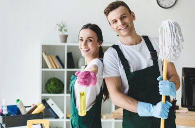 happy-young-cleaners-with-mop-and-spray-bottle-smiling-at-camera-while-cleaning-office-e1616490852654